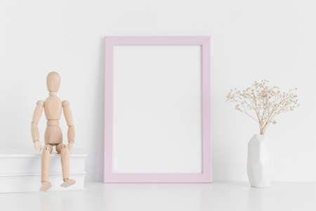 Pink frame mockup with books, manikin and a gypsophila in a vase on a white table.Portrait orientation.の写真素材