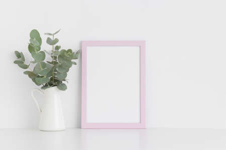 Pink frame mockup with a bouquet of eucalyptus in a vase on a white table.Portrait orientation.の写真素材