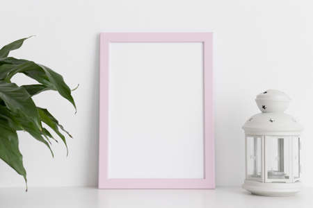 Pink frame mockup with a spathiphyllum and candle holder on a white table. Portrait orientation.の写真素材