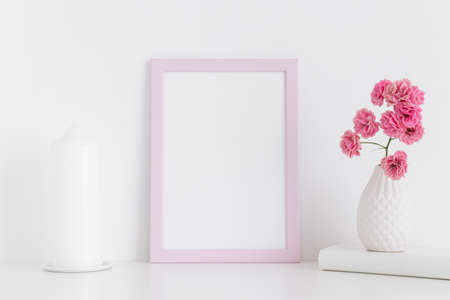 Pink frame mockup with pink roses in a vase and candle on a white table.Portrait orientation.の写真素材