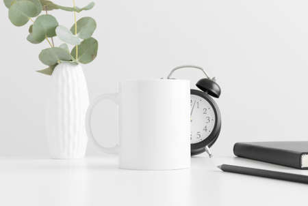 White mug mockup with eucalyptus in a vase and workspace accessories on a white table.の写真素材