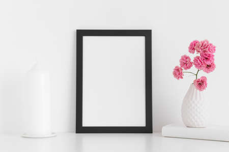 Black frame mockup with pink roses in a vase and candle on a white table.Portrait orientation.の写真素材