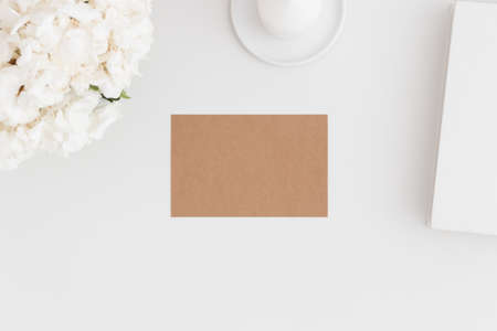 Top view of a craft card mockup with workspace accessories and flowers on a white table.の写真素材