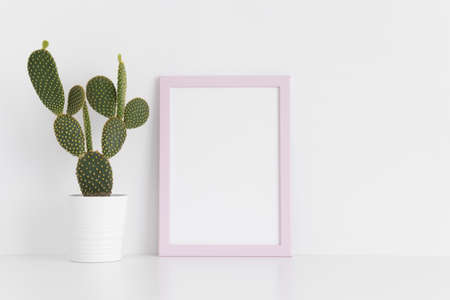 Pink frame mockup with a opuntia cactus in a pot on a white table. Portrait orientation.の写真素材