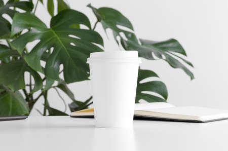 Coffee paper cup mockup  with a monstera plant and a notebook on a white table.の写真素材
