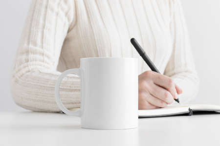 White mug mockup with woman taking notes.の写真素材