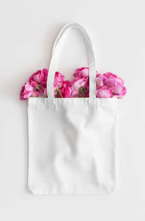 White tote bag mockup with a bouquet of a roses on a white table.の写真素材
