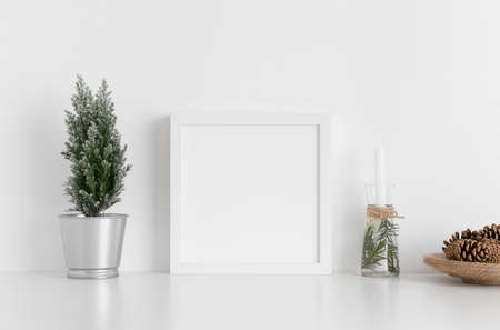 White square frame mockup with a cypress tree, candles and pine cones on a white table. Christmas decoration.の写真素材