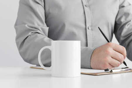 White mug mockup with man taking notes on a clipboard.の写真素材