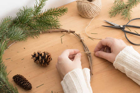 Woman making a christmas wreath with firs and cones on a wooden table.の写真素材