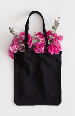 Black tote bag mockup with a bouquet of a roses on a white table.の写真素材