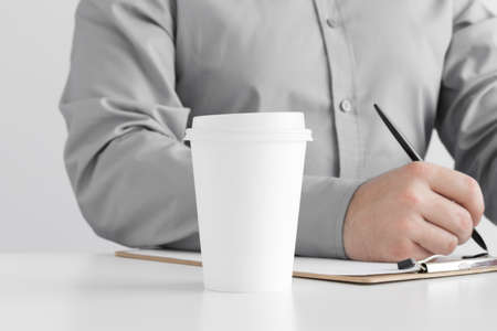 White coffee paper cup mockup with man taking notes on a clipboard.の写真素材