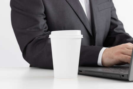 White coffee paper cup mockup with man working on a computer.の写真素材