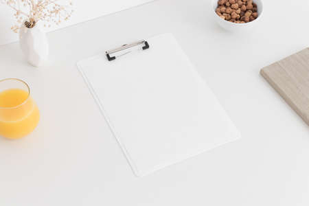 White clipboard mockup wtih a gypsophila in a pot, hazelnuts in a bowl and a juice on a white table.の写真素材