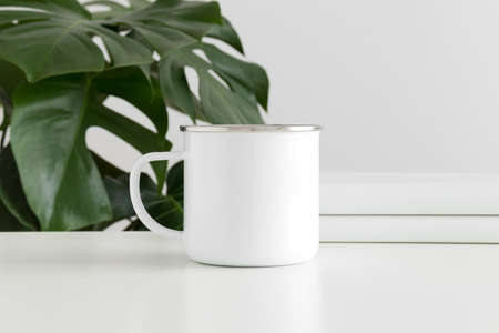 Enamel mug mockup with workspace accessories and a monstera plant.の写真素材