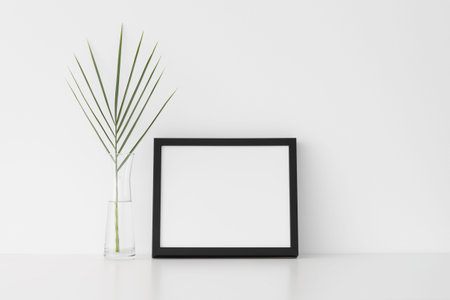 Black frame mockup with palm leaf in a glass vase. Landscape orientation.