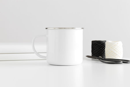 Enamel mug mockup with workspace accessories on a white table.の写真素材