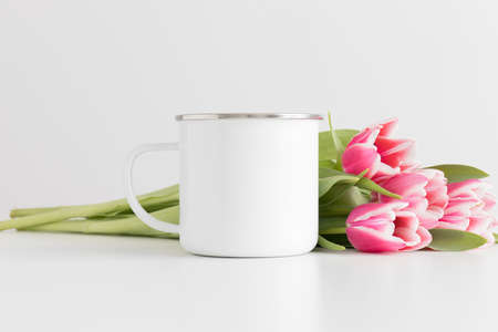 Enamel mug mockup with bouquet of pink tulips on a white table.の写真素材
