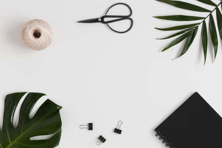 Workspace accessories and tropical leaves on a white table.  Flat lay with blank copy space.の写真素材