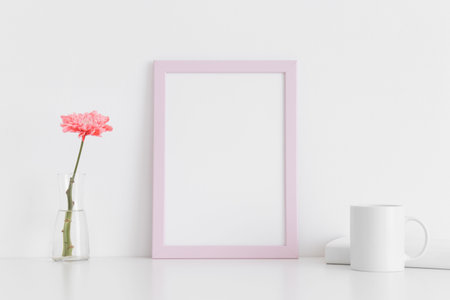 Pink frame mockup with a chrysanthemum in a vase, book and a mug on a white table. Portrait...