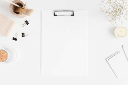 Top view of a white clipboard mockup with a gypsophila in vase and workspace accessories on a white table.の写真素材