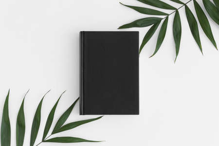 Top view of a black book mockup with palm leaf decoration on a white table.の写真素材