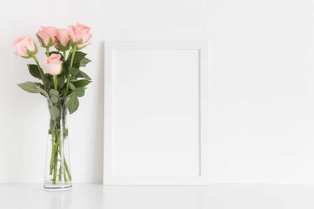 White frame mockup with a bouquet of pink roses in a glass vase on a white table. Portrait orientation.の写真素材