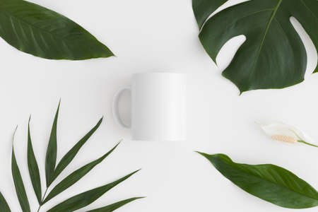 Top view of a white mug mockup with tropical leaves decoration on a white table.の写真素材