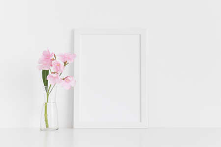 White frame mockup with pink oleander in a glass vase on a white table.Portrait orientation.の写真素材