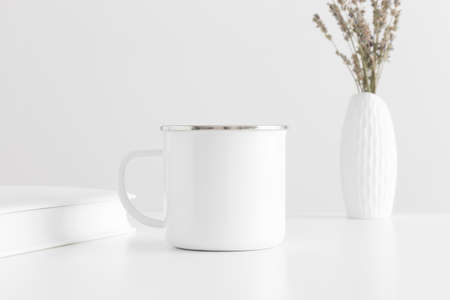 Enamel mug mockup with a lavender in a vase and a book on a white table.の写真素材