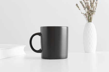 Black mug mockup with a lavender in a vase and a book on a white table.の写真素材