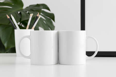 Two mugs mockup with workspace accessories and a monstera plant.の写真素材