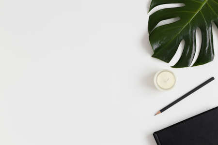 Workspace accessories and a monstera leaf on a white table.  Flat lay with blank copy space.の写真素材