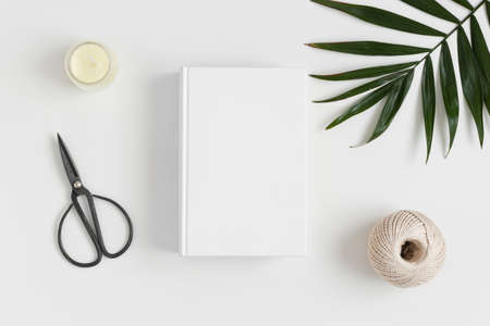 Top view of a white book mockup with  workspace accessories and a palm leaf on a white table.の写真素材