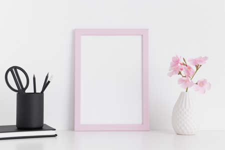 Pink frame mockup with pink oleander in a glass vase and workspace accessories on a white table.Portrait orientation.の写真素材
