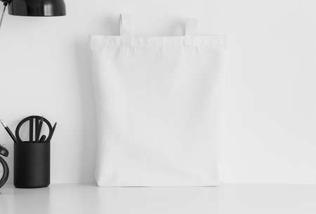 White tote bag mockup with workspace accessories on a white table.の写真素材
