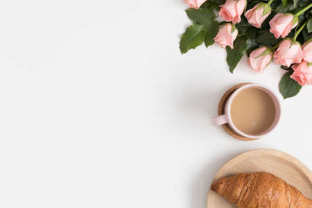Bouquet of pink roses, coffee and a croissant on a white table. Flat lay with blank copy space.の写真素材