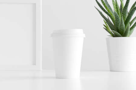 Coffee paper cup mockup with a cactus in a pot and a frame on a white table.の写真素材