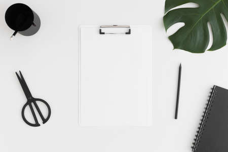Top view of a white clipboard mockup with  workspace accessories and a monstera leaf on a white table.の写真素材