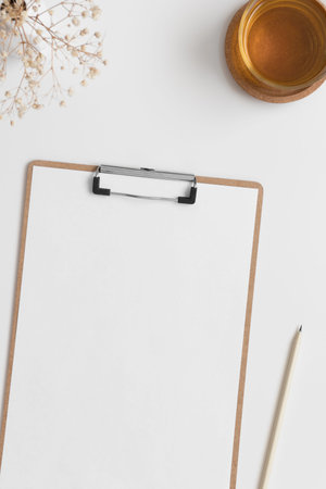 Wooden clipboard mockup with a cup of tea and gypsophila on a white table.