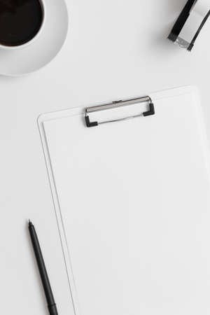 White clipboard mockup with a cup of coffee and workspace accessories on a white table.の写真素材