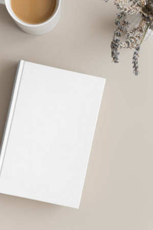 White book mockup with a cup of coffee and lavender on a beige table.