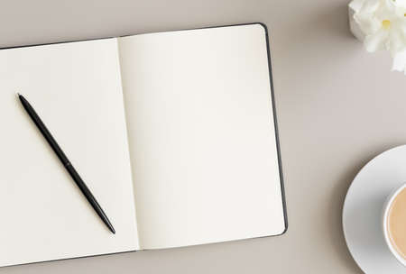 Open notebook mockup with a cup of coffee and oleander on a beige table.の写真素材