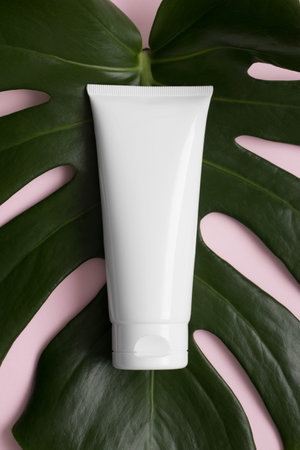 Top view of a white tube of cream mockup with a monstera leaf on a pink background.