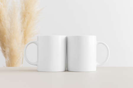 Two white mugs mockup on a beige table with pampas decoration.の写真素材