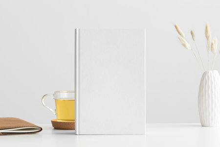 White book mockup with a lagurus and workspace accessories on a white table.の写真素材