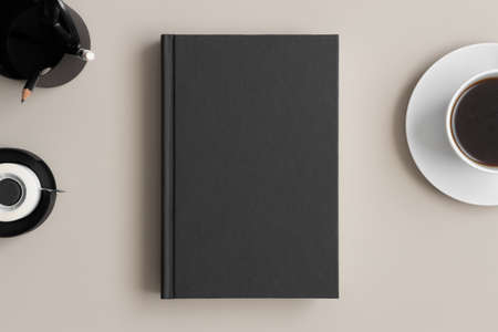 Black book mockup with a coffee and workspace accessories on a beige table.の写真素材