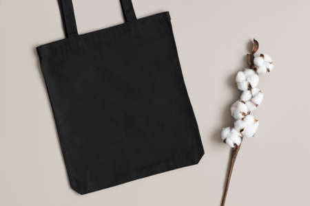 Black tote bag mockup with a cotton branch decoration on the beige background.の写真素材