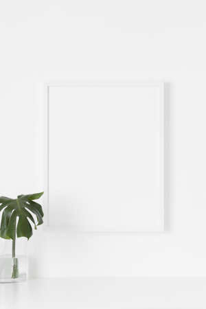 White frame mockup on the wall with a  monstera leaf in a glass vase.の写真素材
