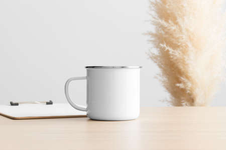 Enamel mug mockup with a clipboard on the wooden table with a pampas decoration.の写真素材
